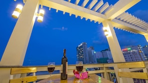 A terrace with a view of the city skyline at dusk, featuring a bottle of wine and glasses on a table. - Dam Tien Hotel (Da Nang)