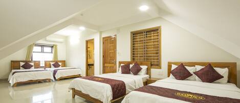 Habitación de hotel con tres camas, cada una con cabecero de madera y ropa de cama blanca.