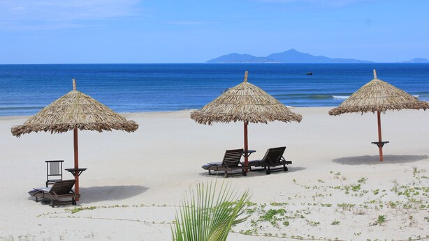 A beach with three thatched umbrellas and lounge chairs. - Dam Tien Hotel (Da Nang)