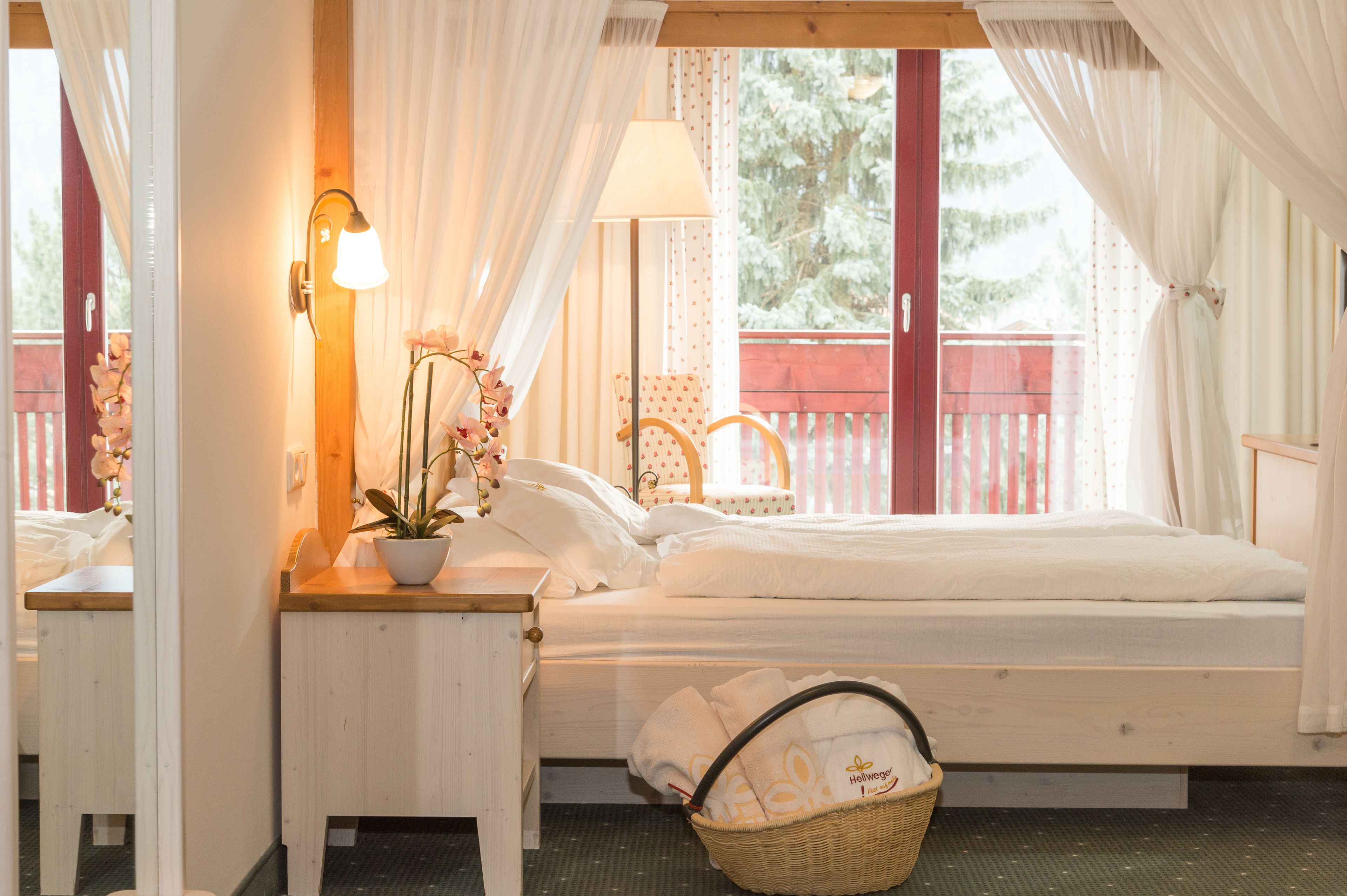 A bedroom with a bed, a nightstand with a lamp, a potted plant, and a wicker basket.