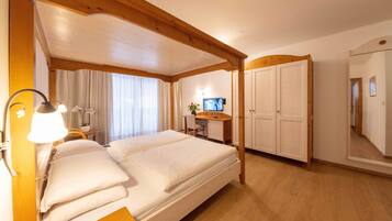 Habitación de hotel con una cama grande, un escritorio, una silla, un televisor y un armario.