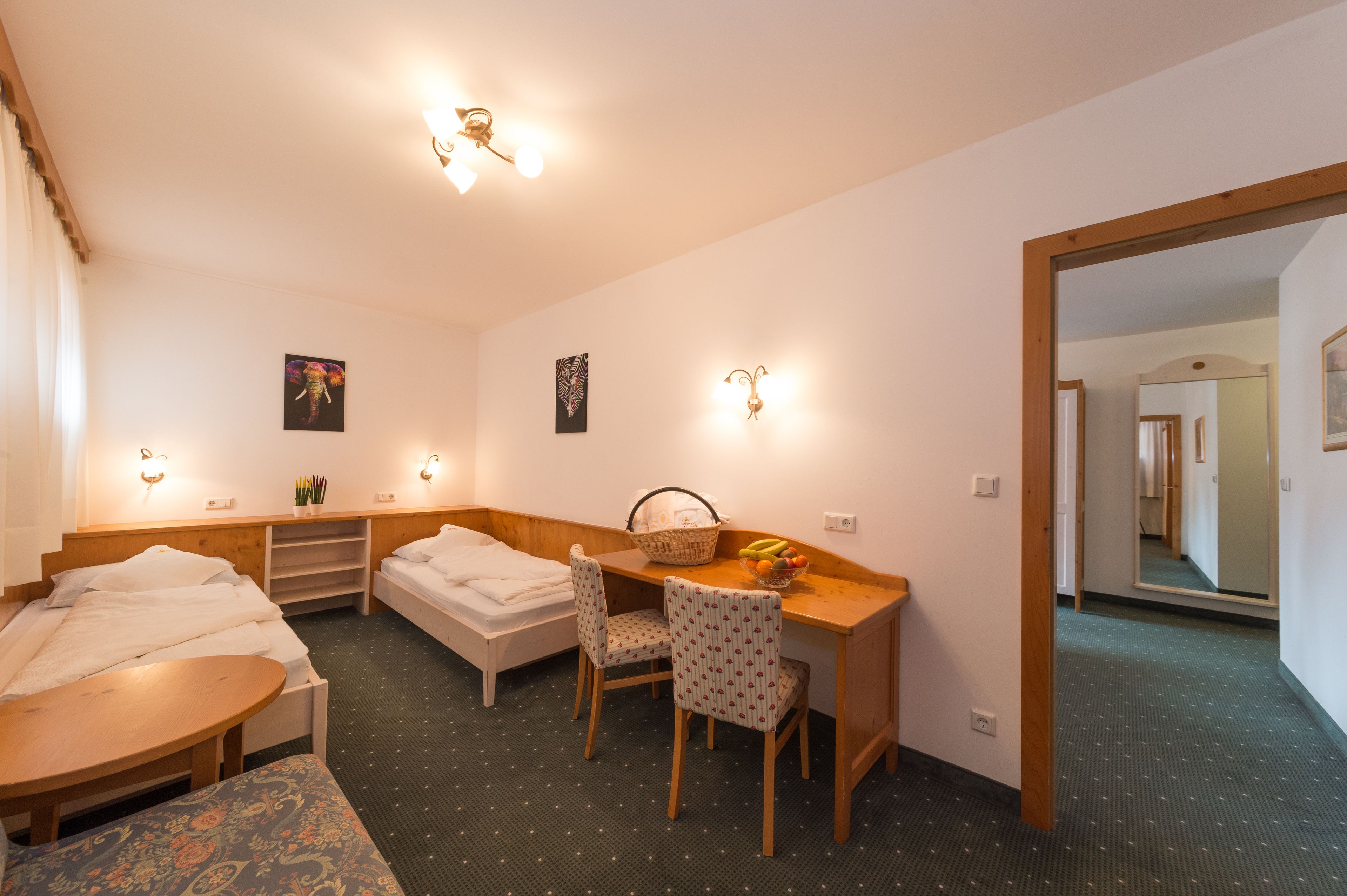 A compact hotel room with a bed, a desk with a chair, a small table, and a mirror.