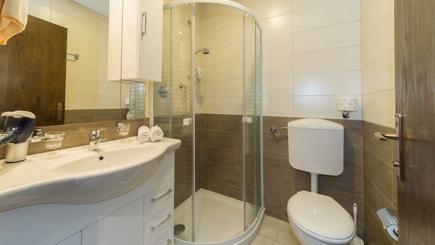 Ein modernes Badezimmer mit einer Duschkabine aus gebogenem Glas, einem weißen Waschbecken mit Spiegel darüber und einem WC mit Tank.