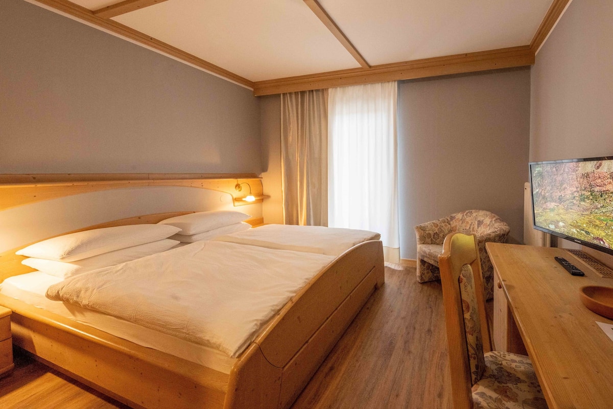A hotel room with a double bed, bedside lamps, a TV, a wooden desk, and a chair.