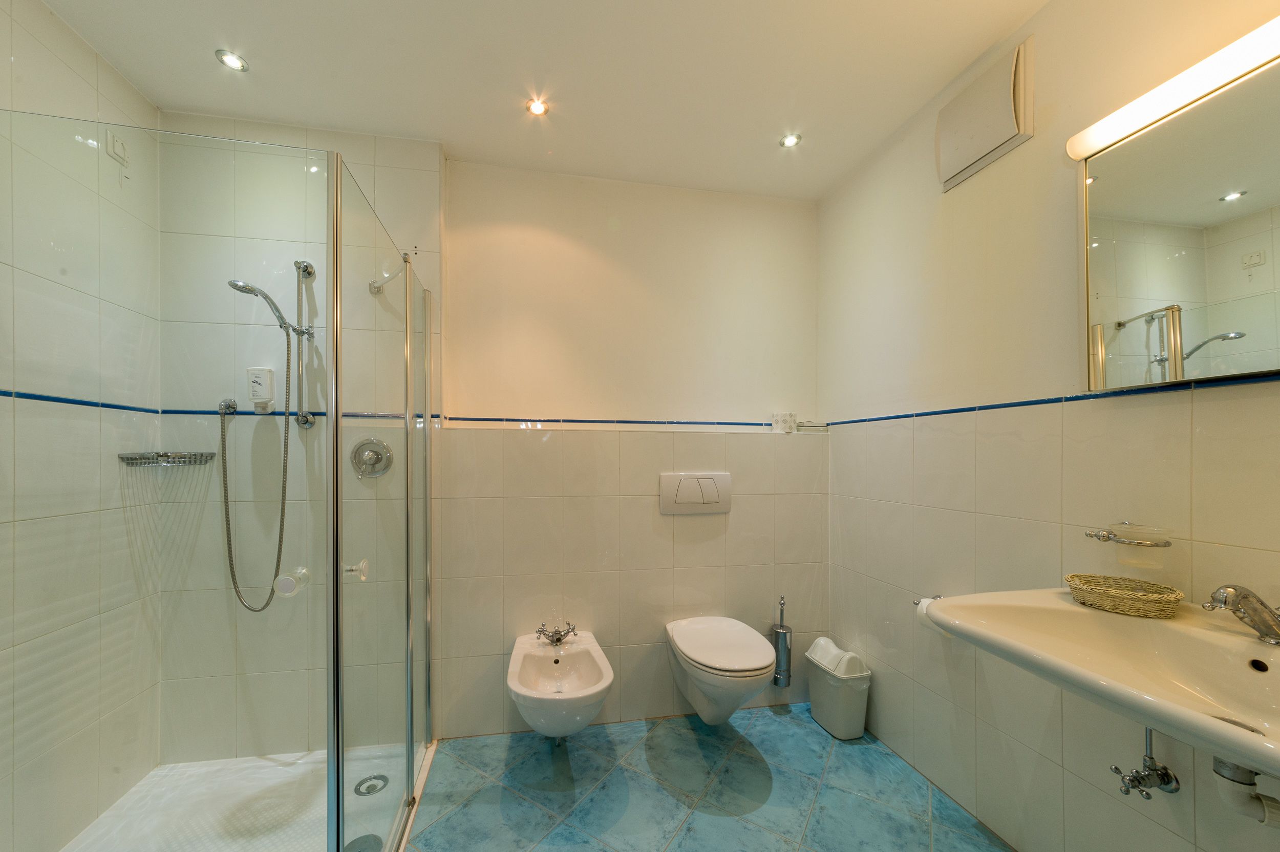 Une salle de bain moderne dotée d’une douche à parois de verre, d’un bidet, de toilettes et d’un lavabo avec un miroir au-dessus.