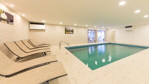 Ein Hallenbad mit Liegestühlen und Blick ins Freie.