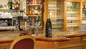 Eine Bar mit einer Kaffeemaschine, Regalen voller Spirituosenflaschen und einem Weinglasständer.