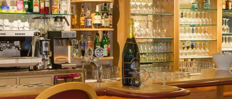 Un espace bar équipé d’une machine à café, d’étagères remplies de bouteilles d’alcool et d’un porte-verres à vin.