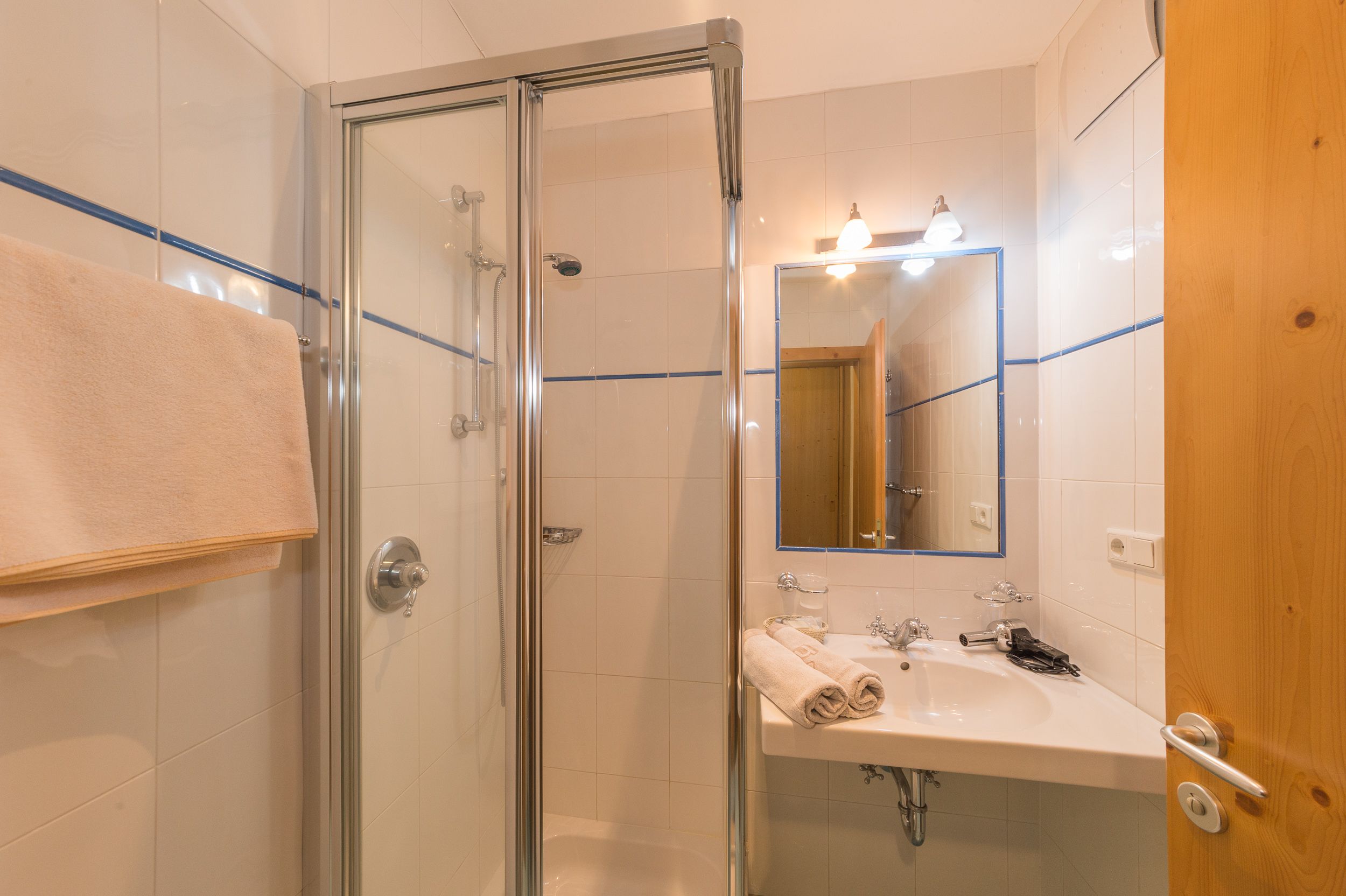 A modern bathroom with a glass-enclosed shower, a white sink, and a mirror with lights.