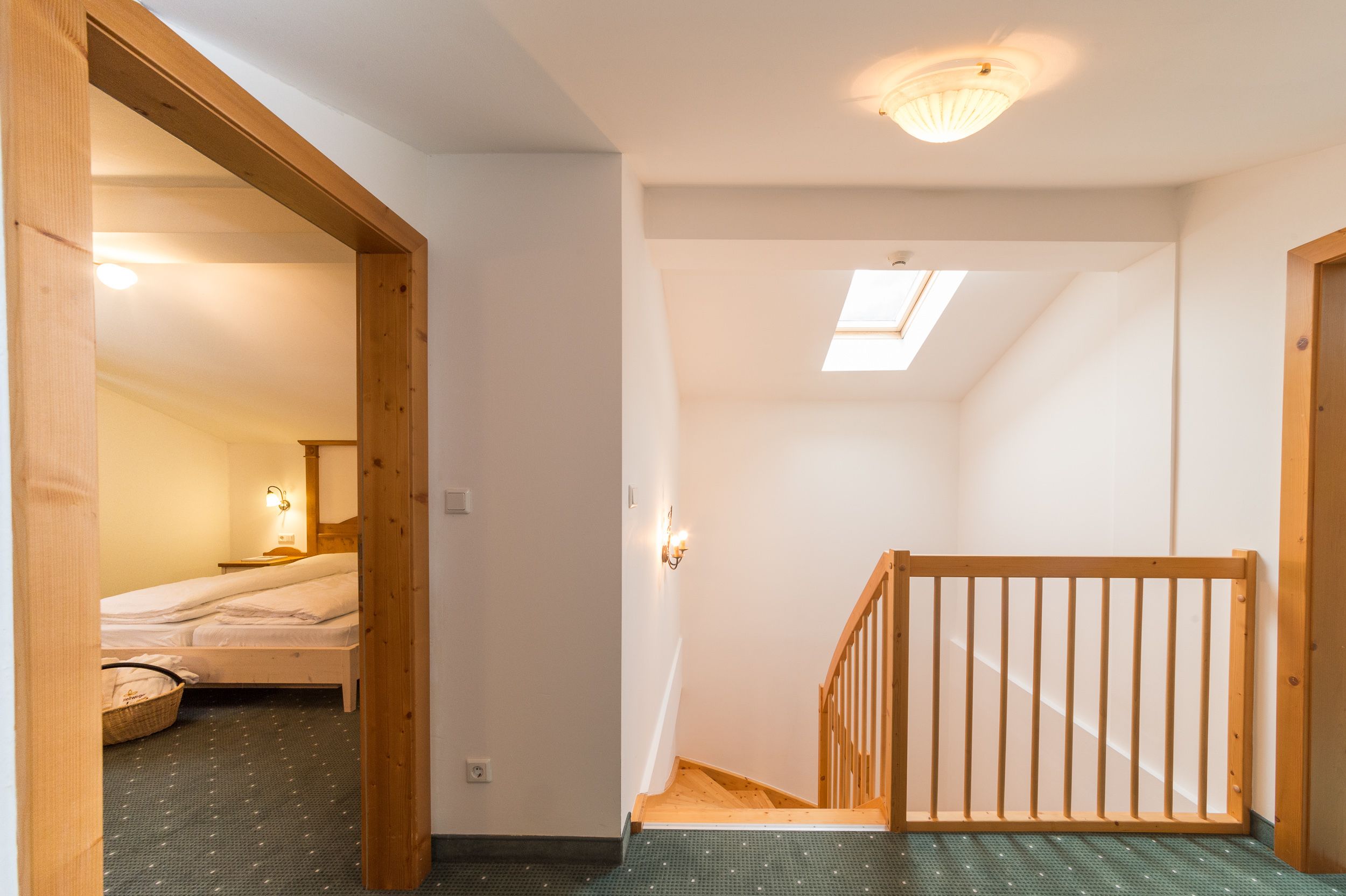 A narrow staircase with a wooden handrail leading to a room with a bed and a nightstand.