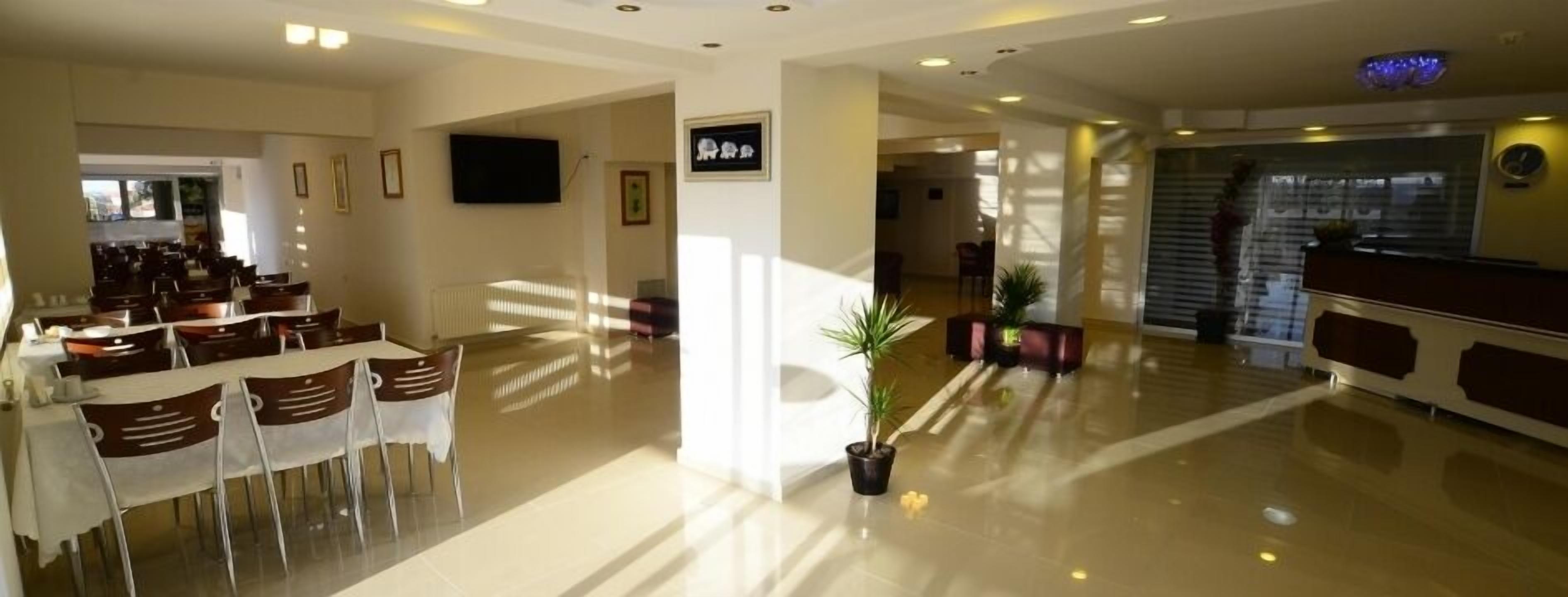 A hotel lobby with a reception desk, a dining area with tables and chairs, and a large potted plant.