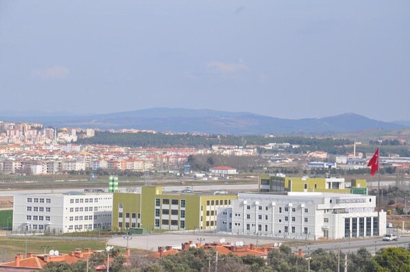 A modern building complex with multiple white and green buildings, a flag, and a view of a cityscape with mountains in the background.