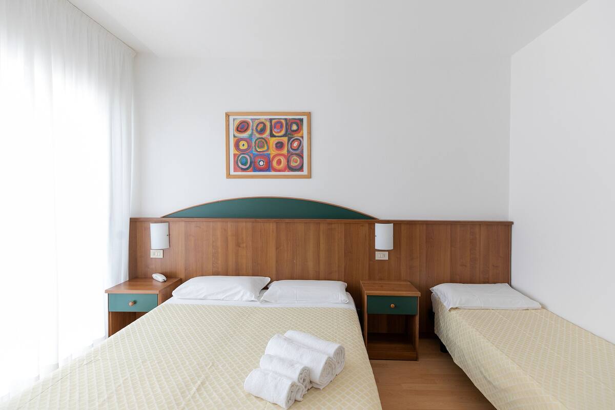 A hotel room with two beds, wooden headboards, bedside tables, and a wall-mounted artwork.