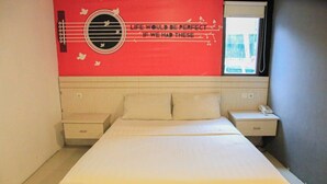 Un dormitorio con una cama, dos mesitas de noche, una mesita auxiliar, una ventana con vistas y una decoración en la pared.