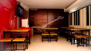 Un restaurante con mesas y bancos de madera, una pared roja con una cita y un mural de una guitarra.