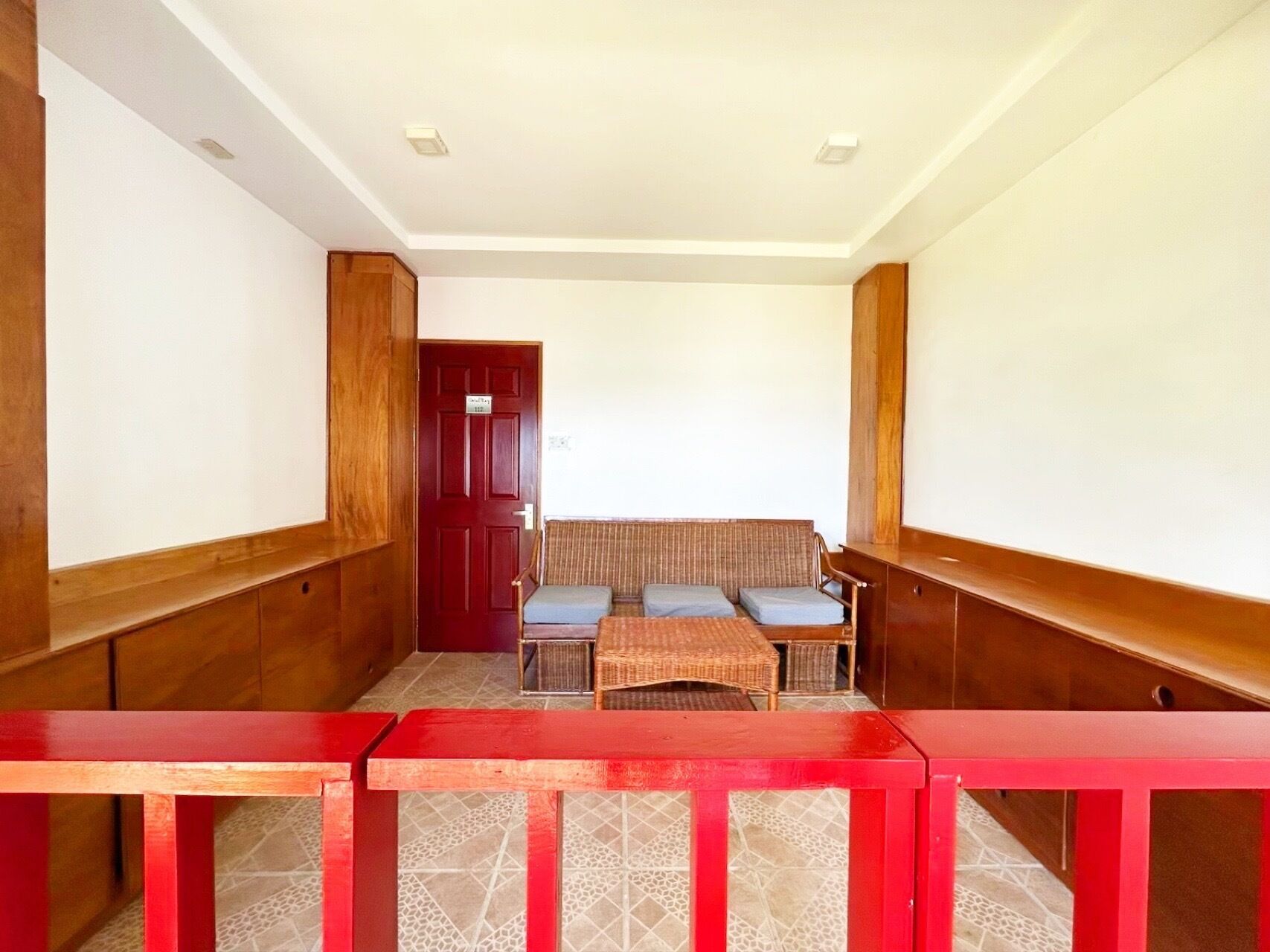 Una stanza con una panca in legno, un tavolo rosso e una porta con un cartello.
