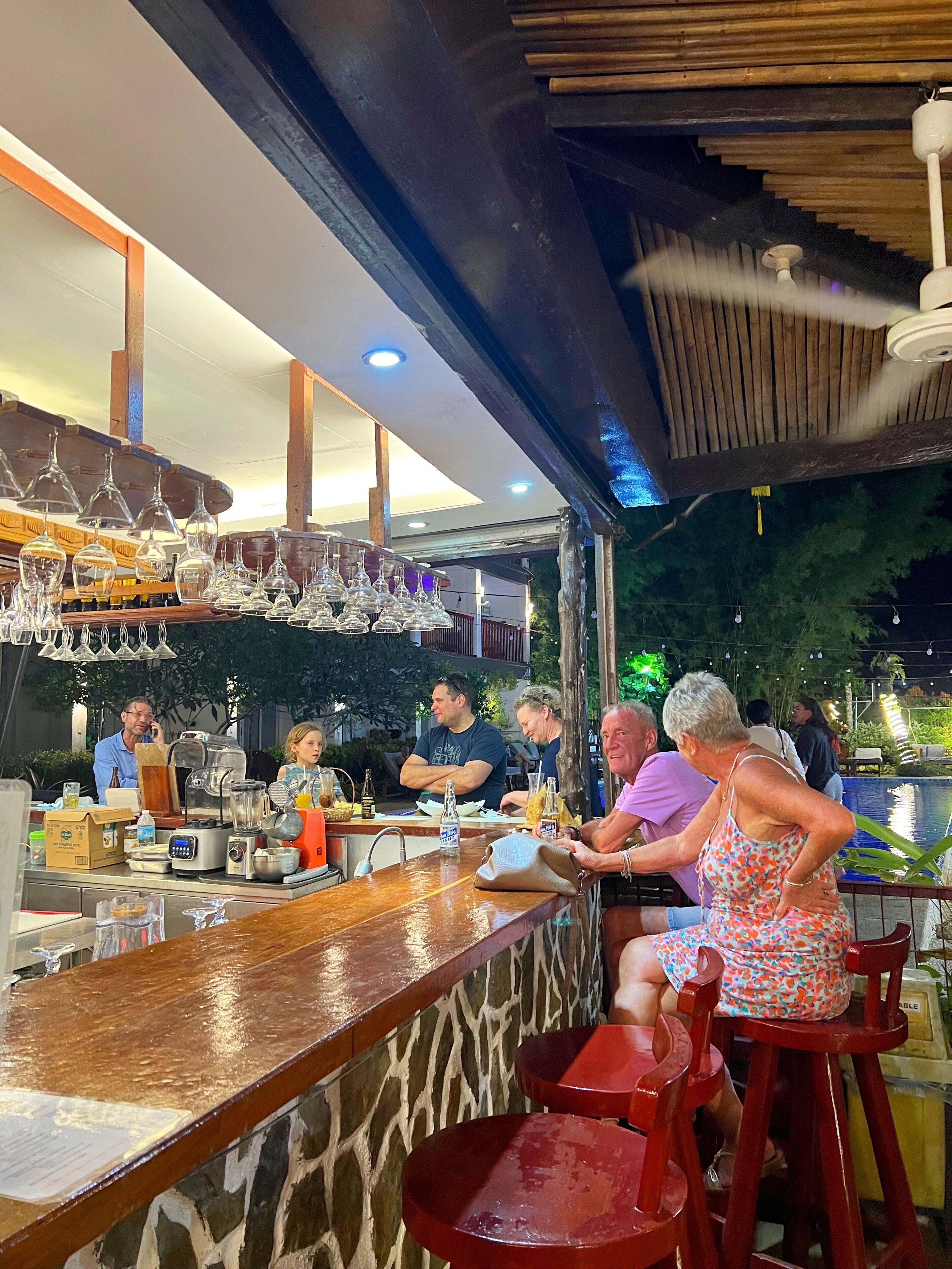 Una zona de bar con taburetes, una barra y copas colgando.