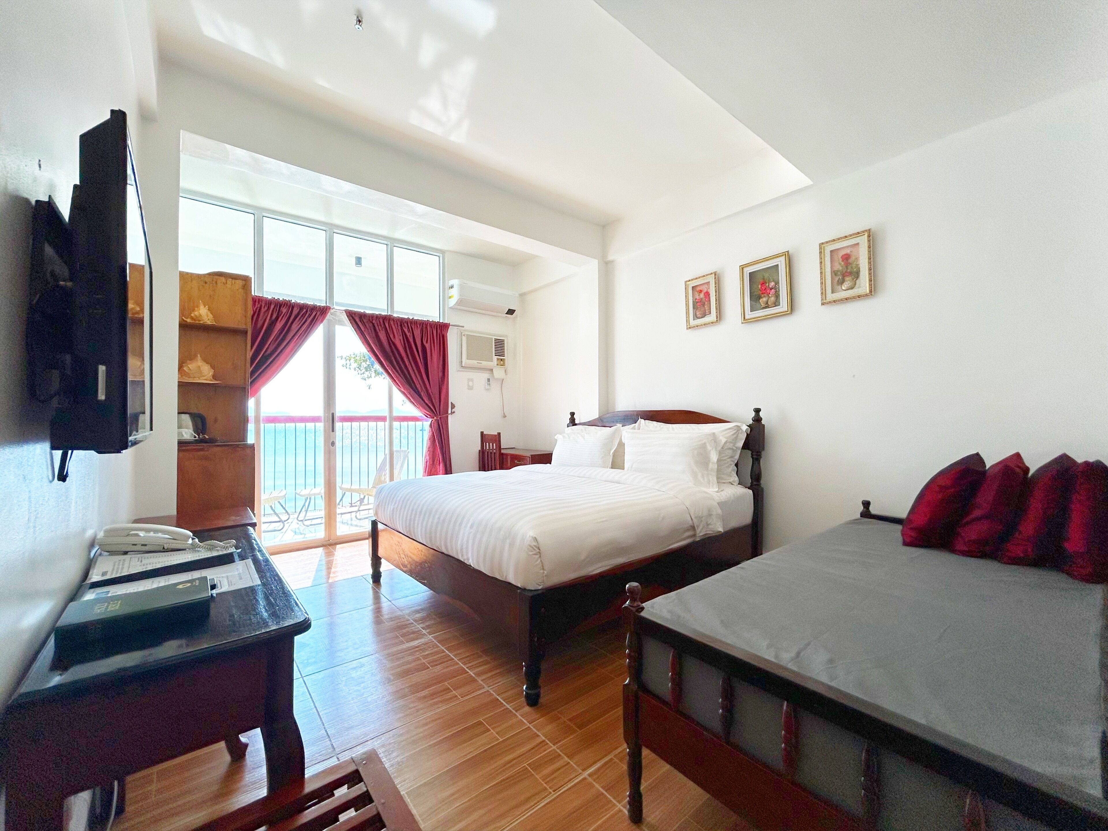 Habitación de hotel con cama, escritorio con teléfono, silla, armario y balcón con cortinas rojas.