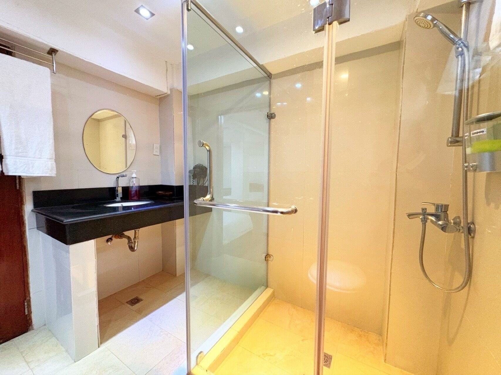 A modern bathroom with a glass-enclosed shower, a black countertop sink, and a round mirror.