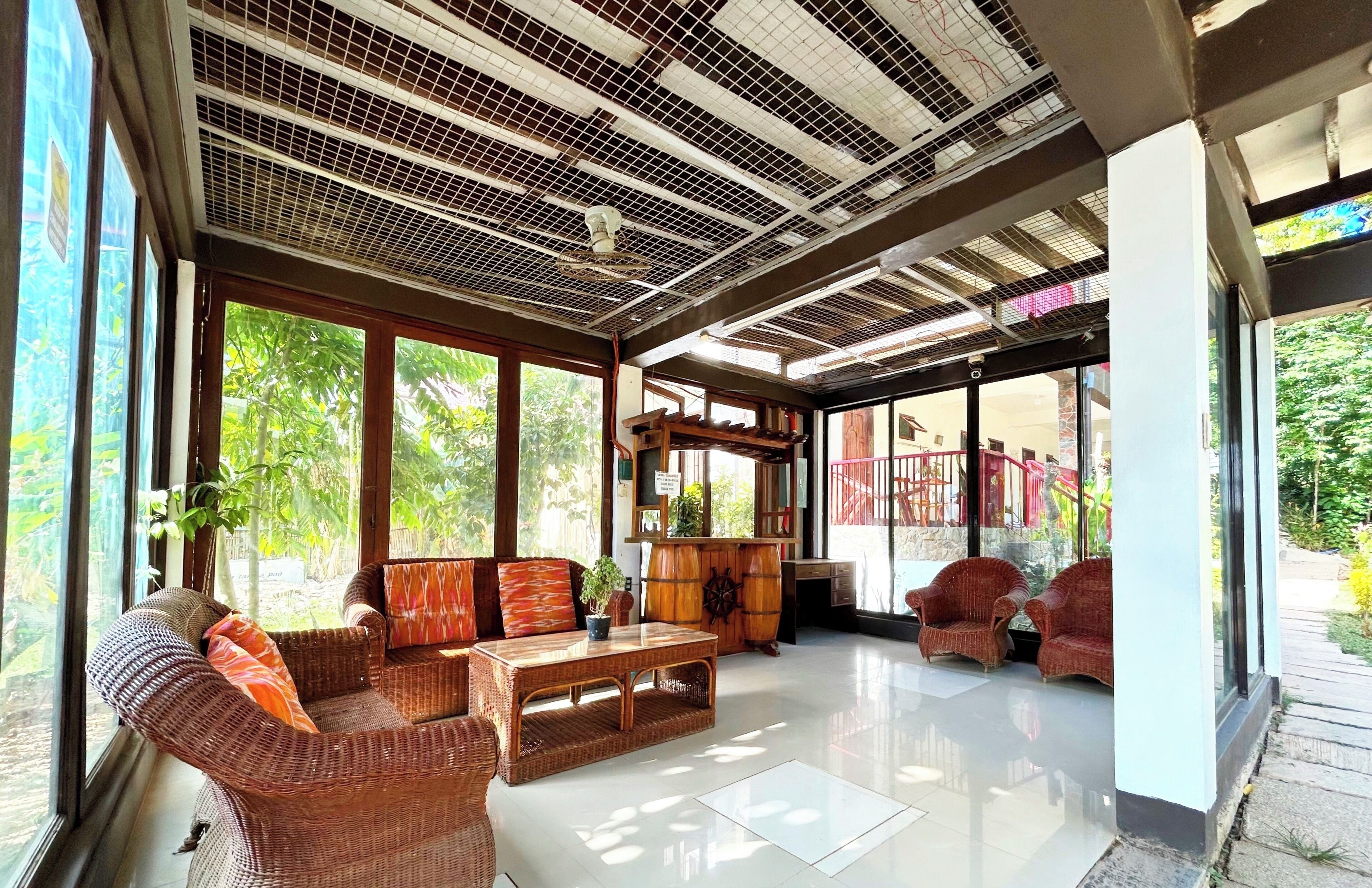Una habitación amplia con ventanas grandes, mobiliario de mimbre y un techo con diseño de cuadrícula.