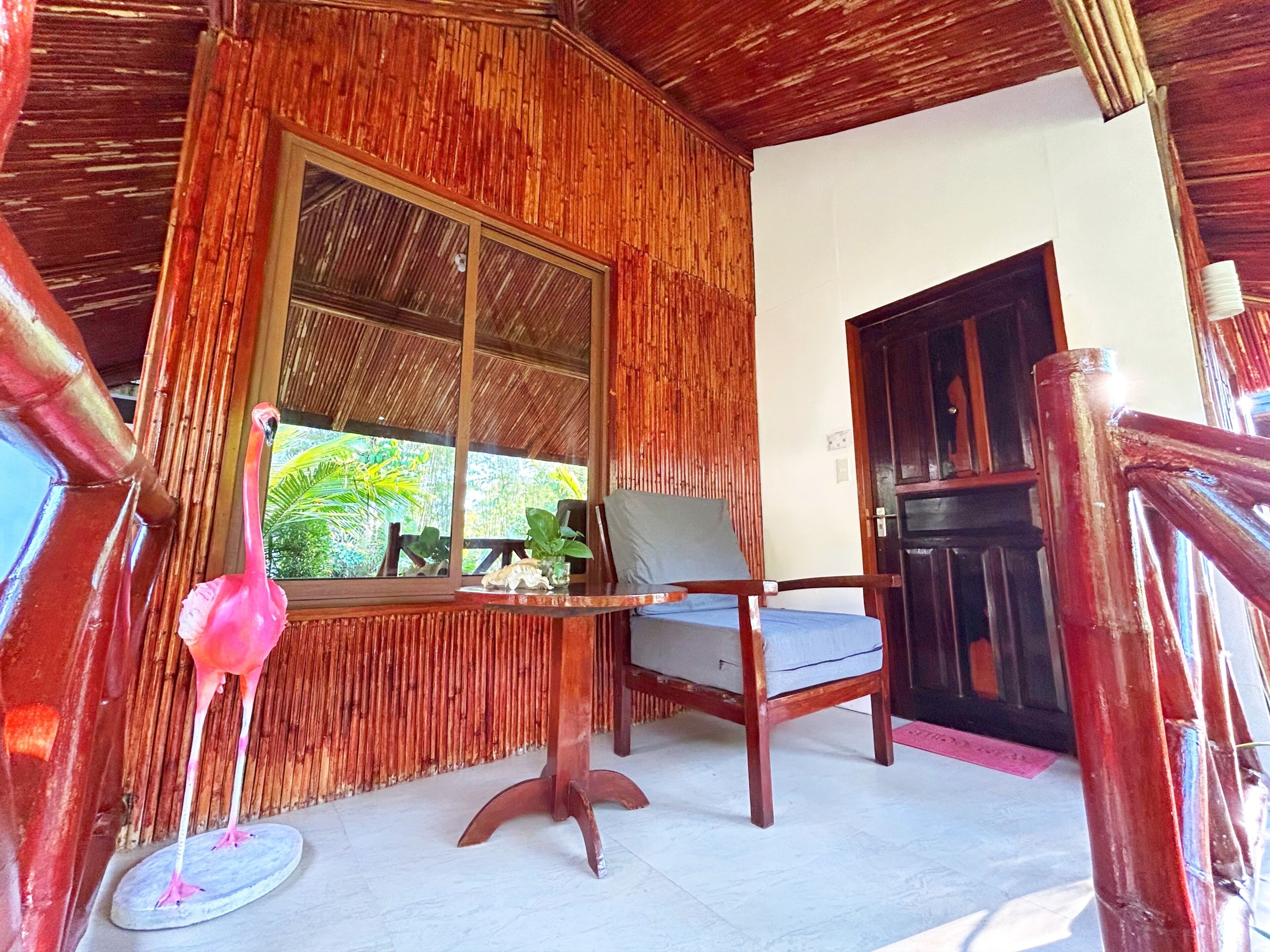 Une pièce avec un plafond en bois, une fenêtre donnant sur la verdure, une chaise et une porte.