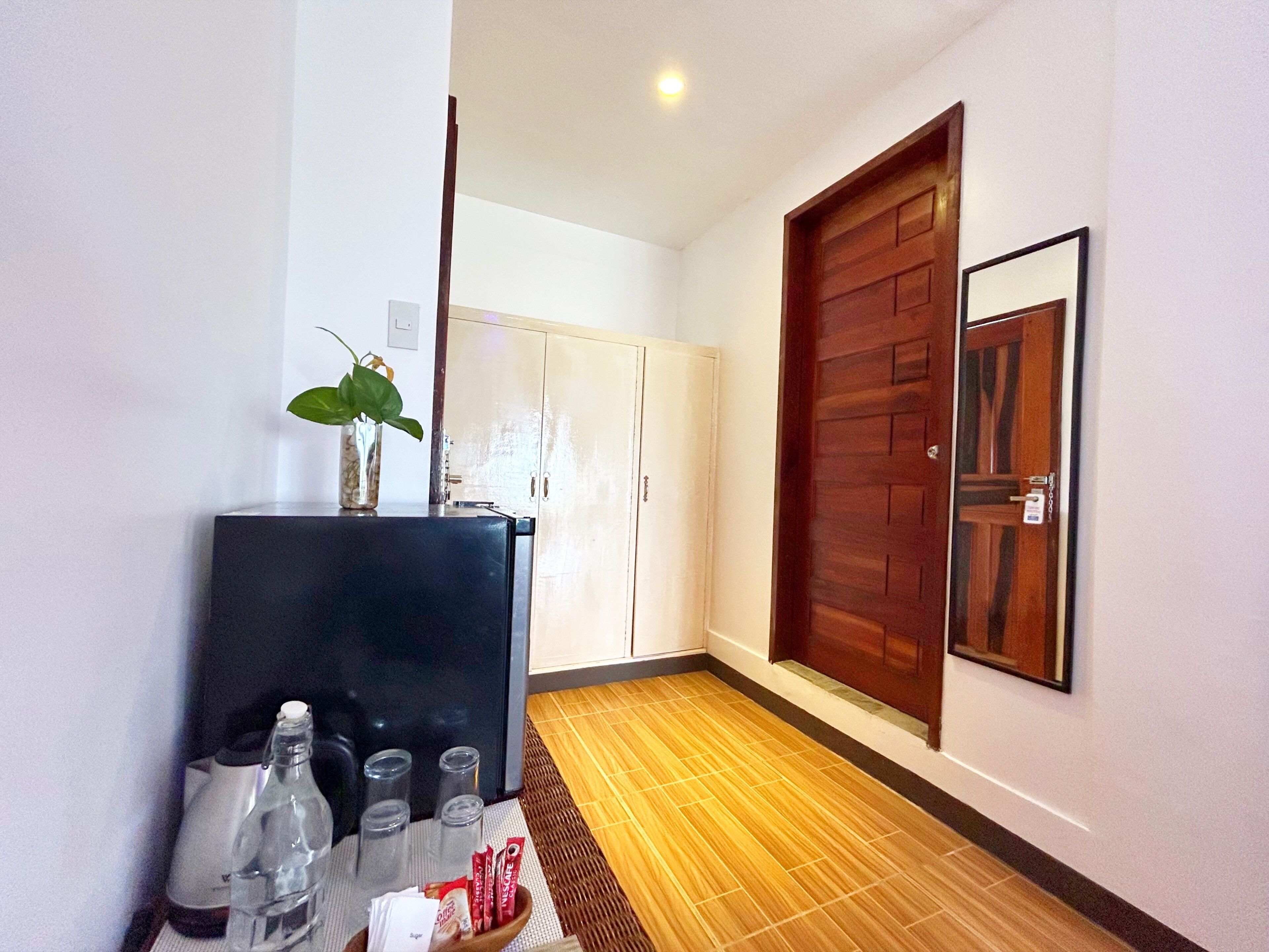 Habitación de hotel con minibar, puerta de madera, espejo y suelo de baldosas.