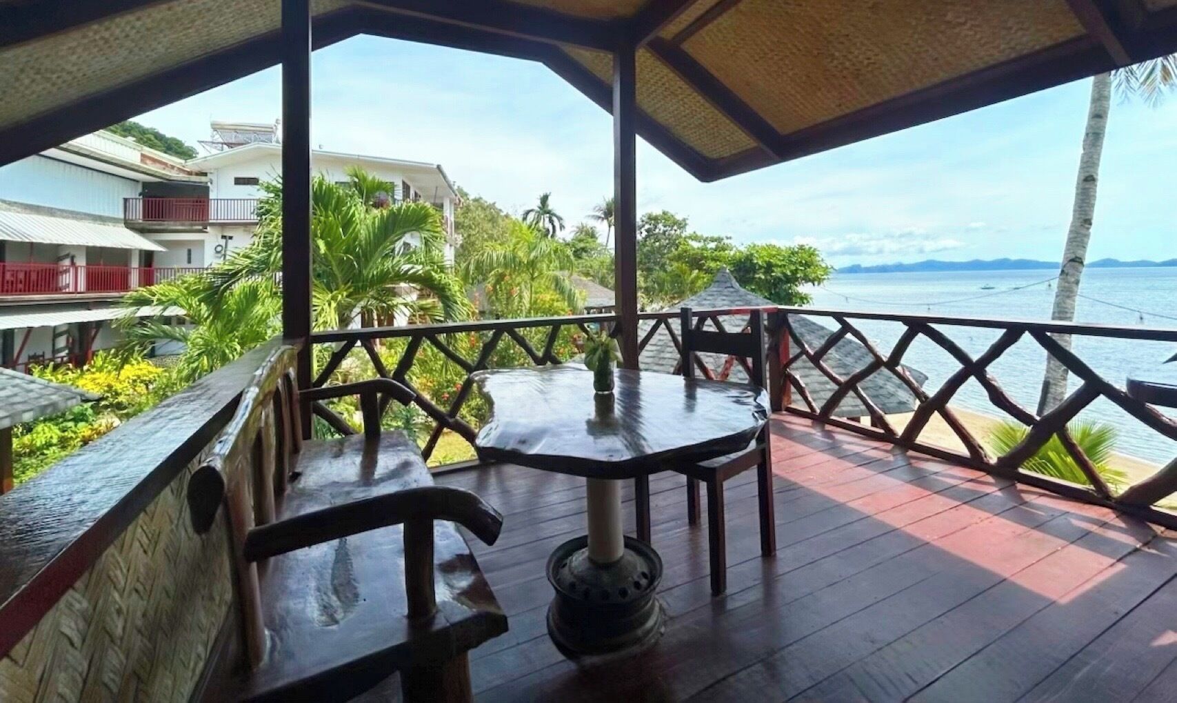 A covered outdoor seating area with tables and chairs, overlooking a body of water and a view of buildings in the background.