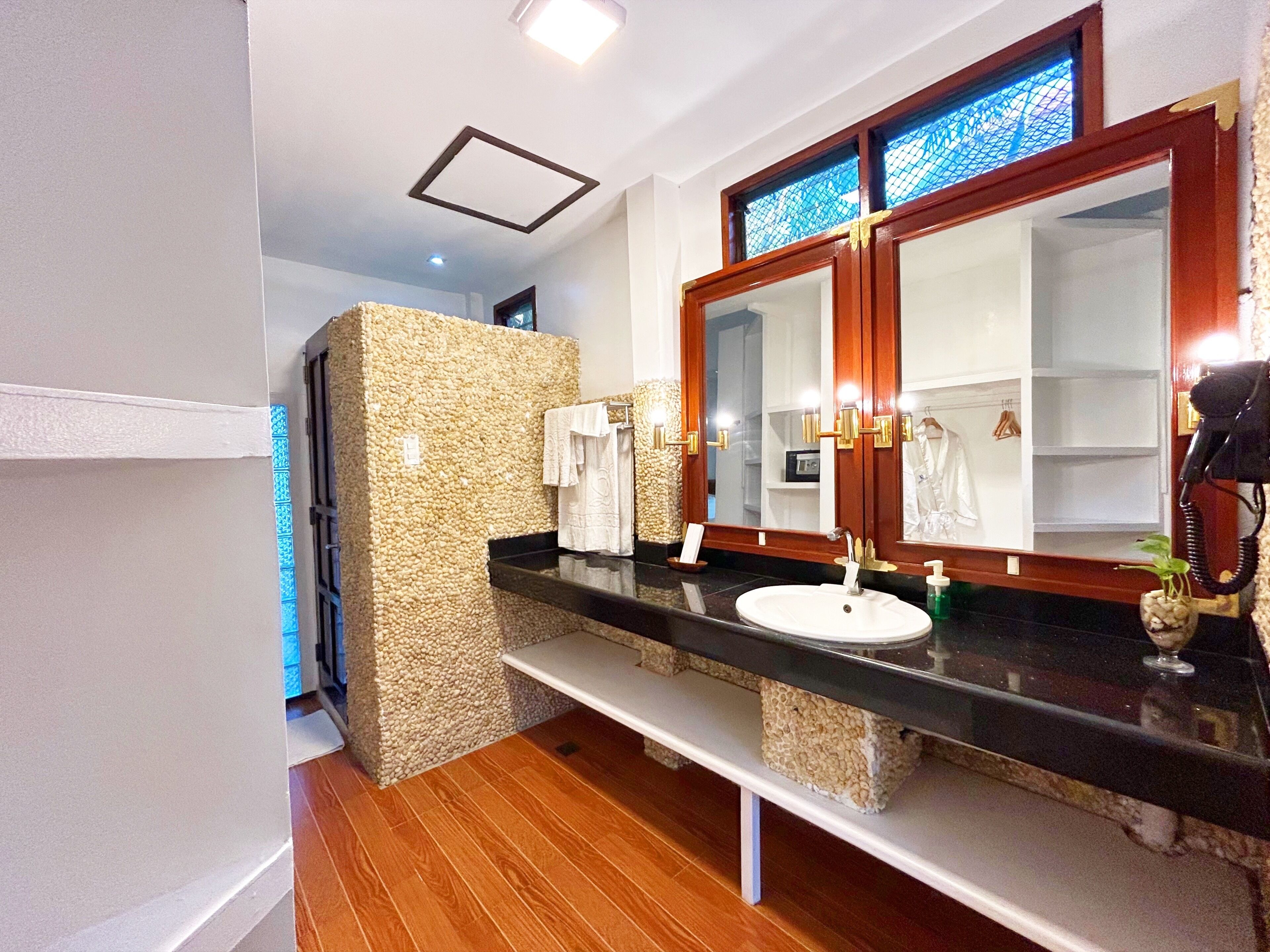 Une salle de bain avec un grand miroir, un lavabo, un banc et un mur en pierre.