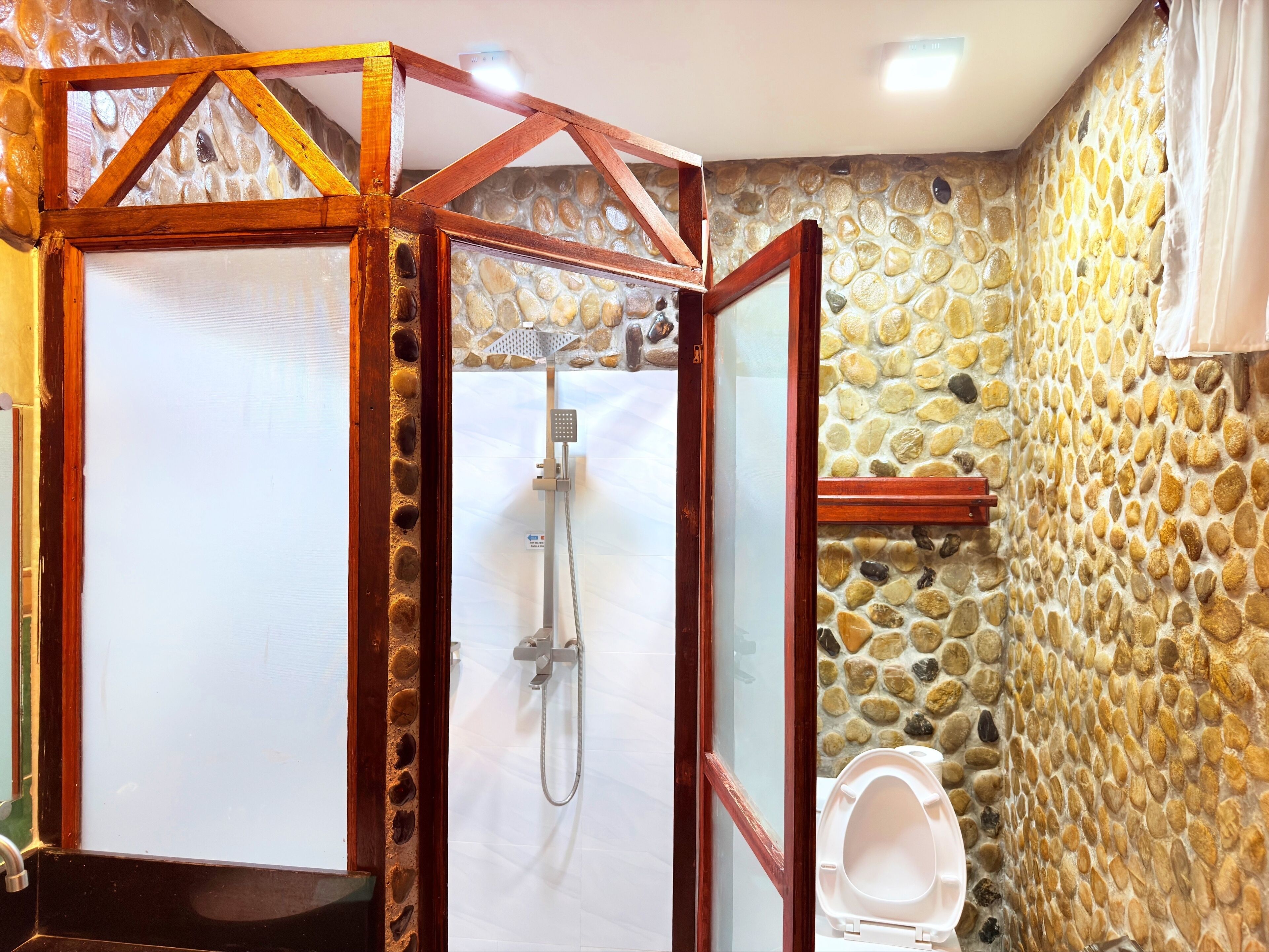 Un baño con pared de piedra, cabina de ducha con marco de madera y un inodoro.