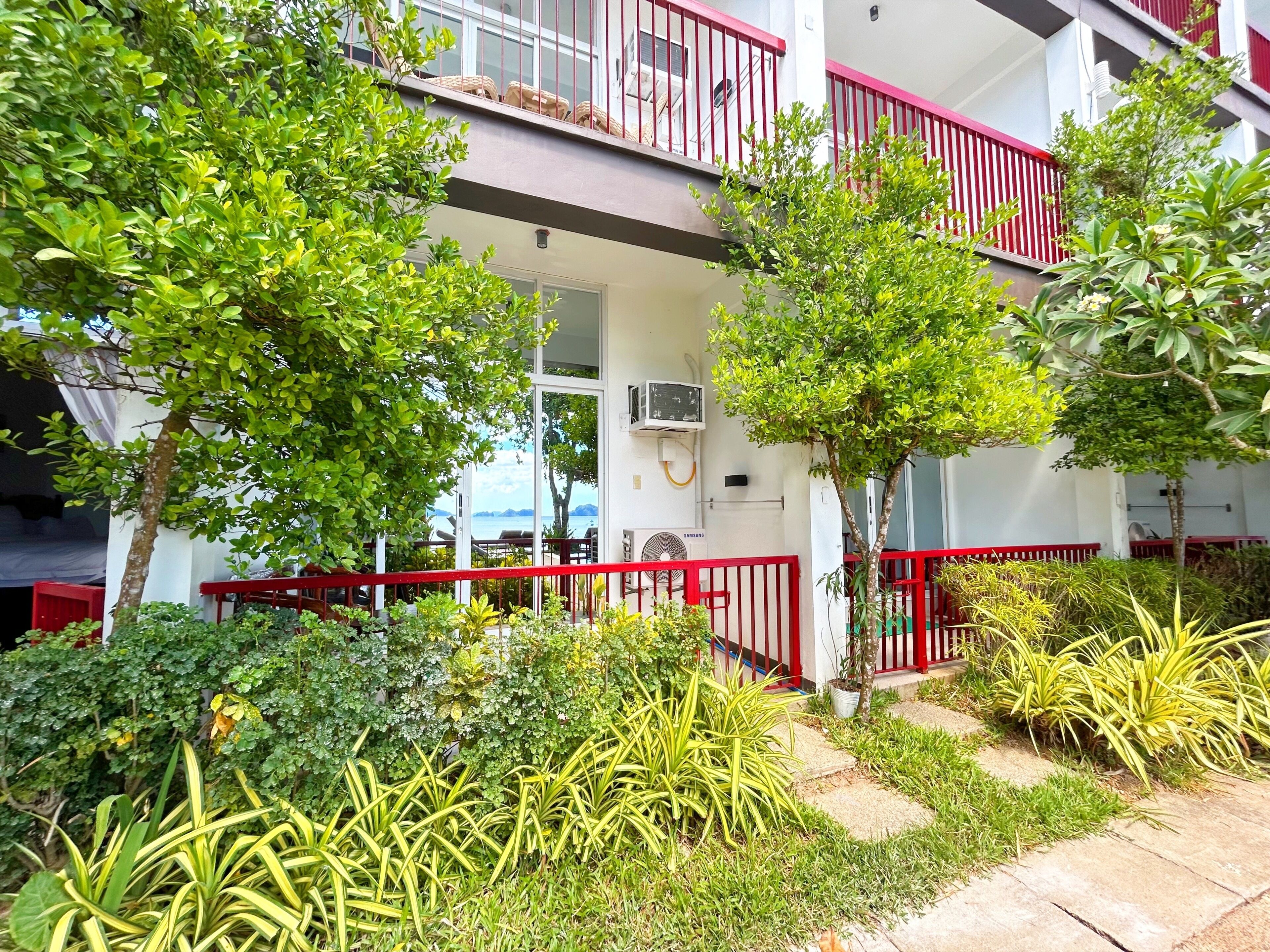 A building with a red balcony railing, a door with a glass panel, and a view of the sea.