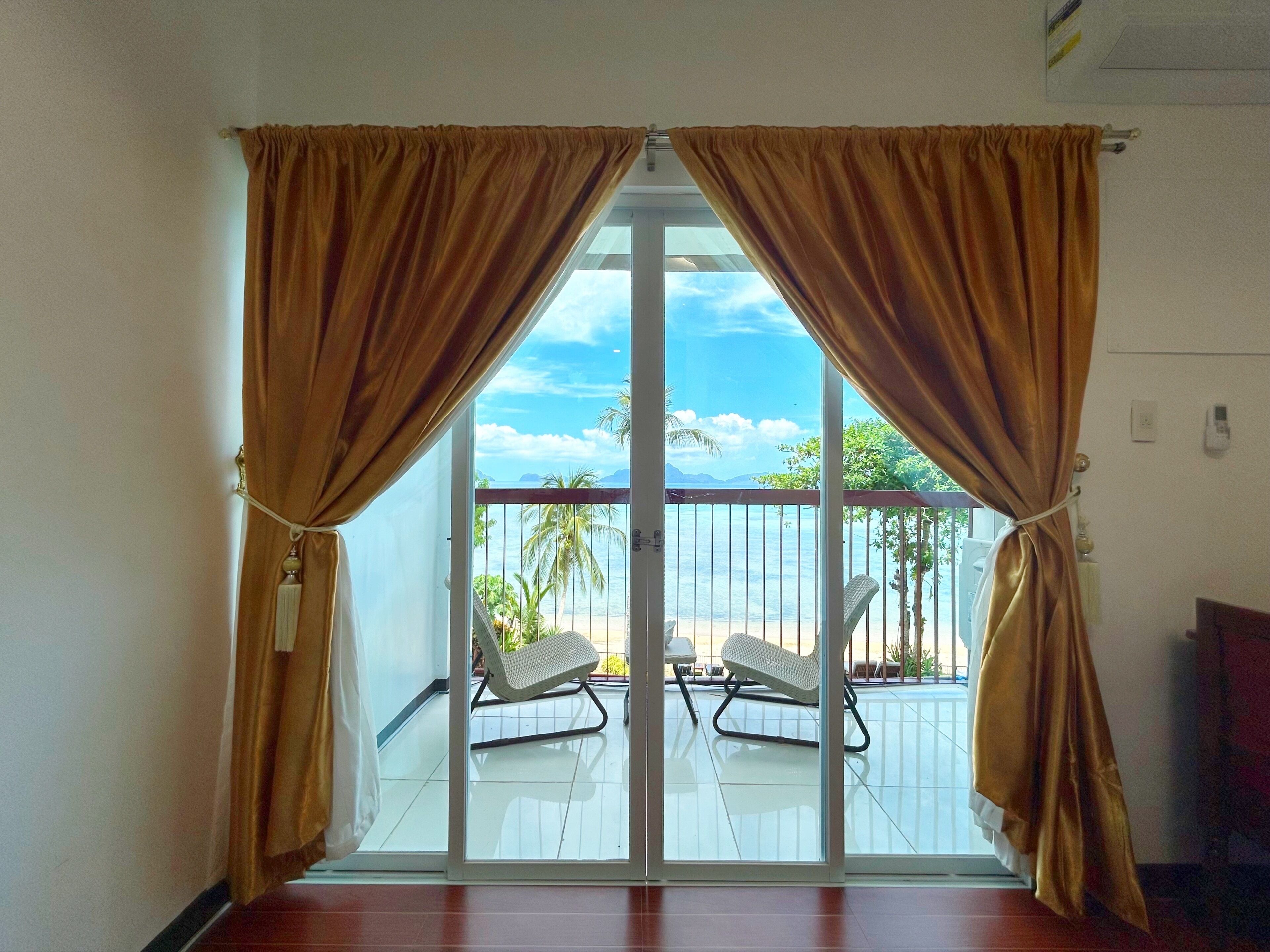 A room with a sliding glass door leading to a balcony with two lounge chairs and a view of the sea.