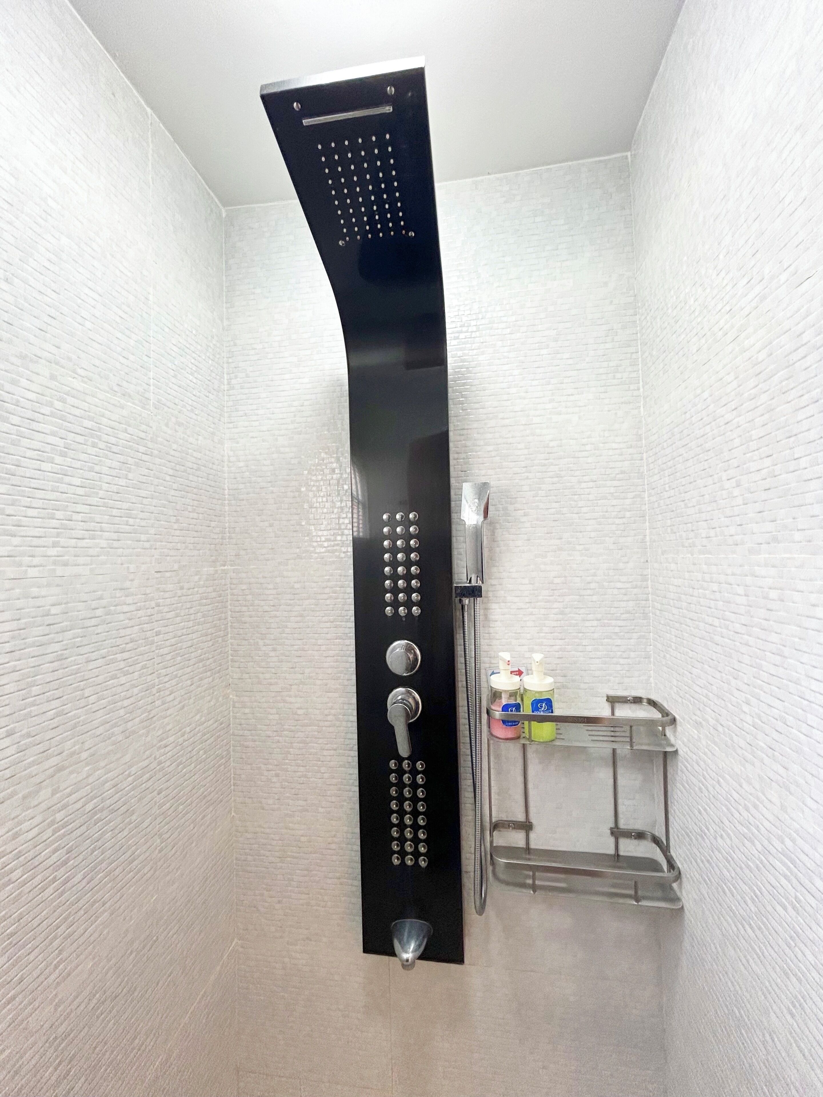 Een moderne douche met bedieningspaneel, douchekop en een klein plankje met toiletartikelen.