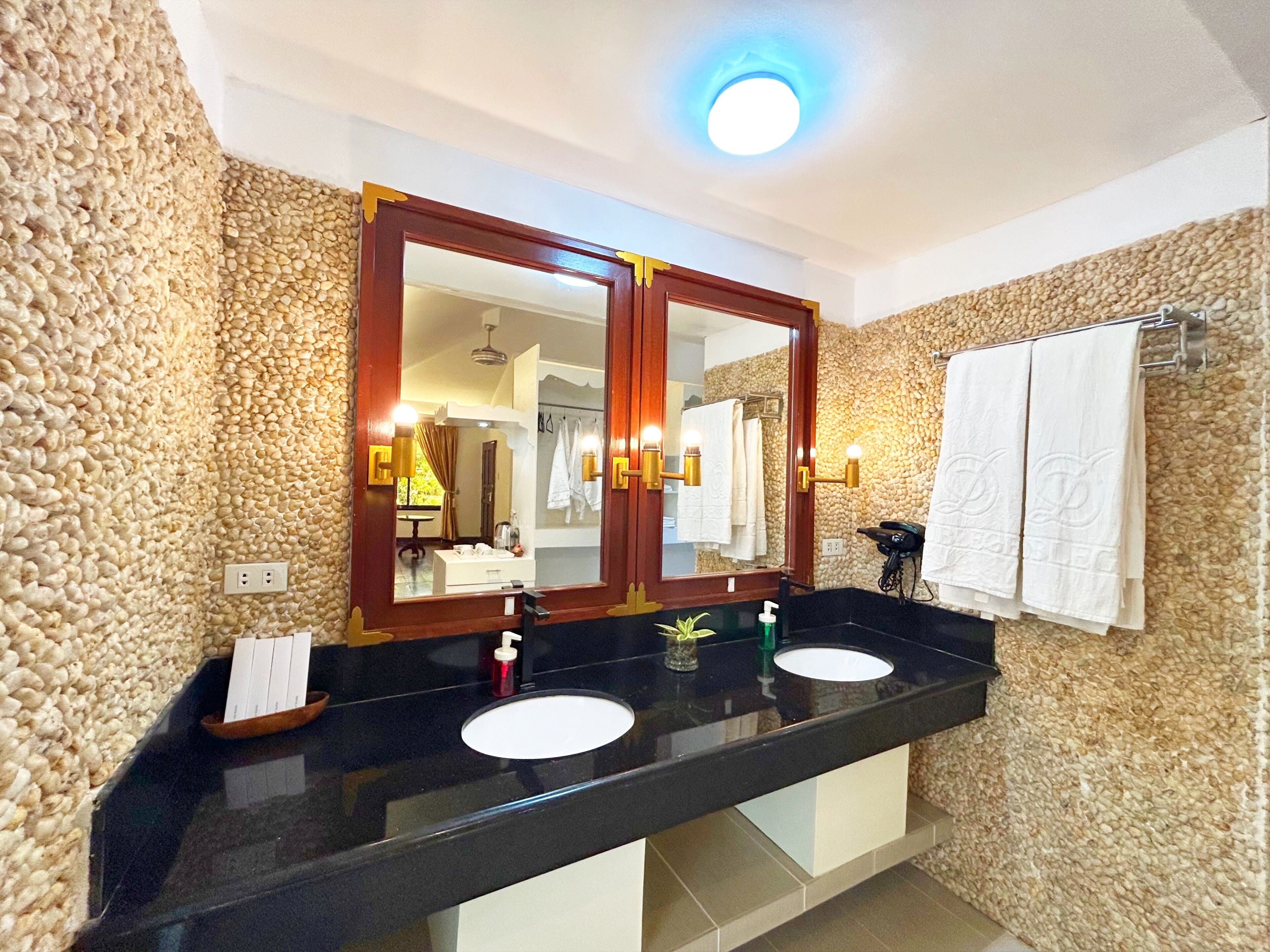 A bathroom with a double sink, two mirrors, a ceiling light, and towels on a rack.
