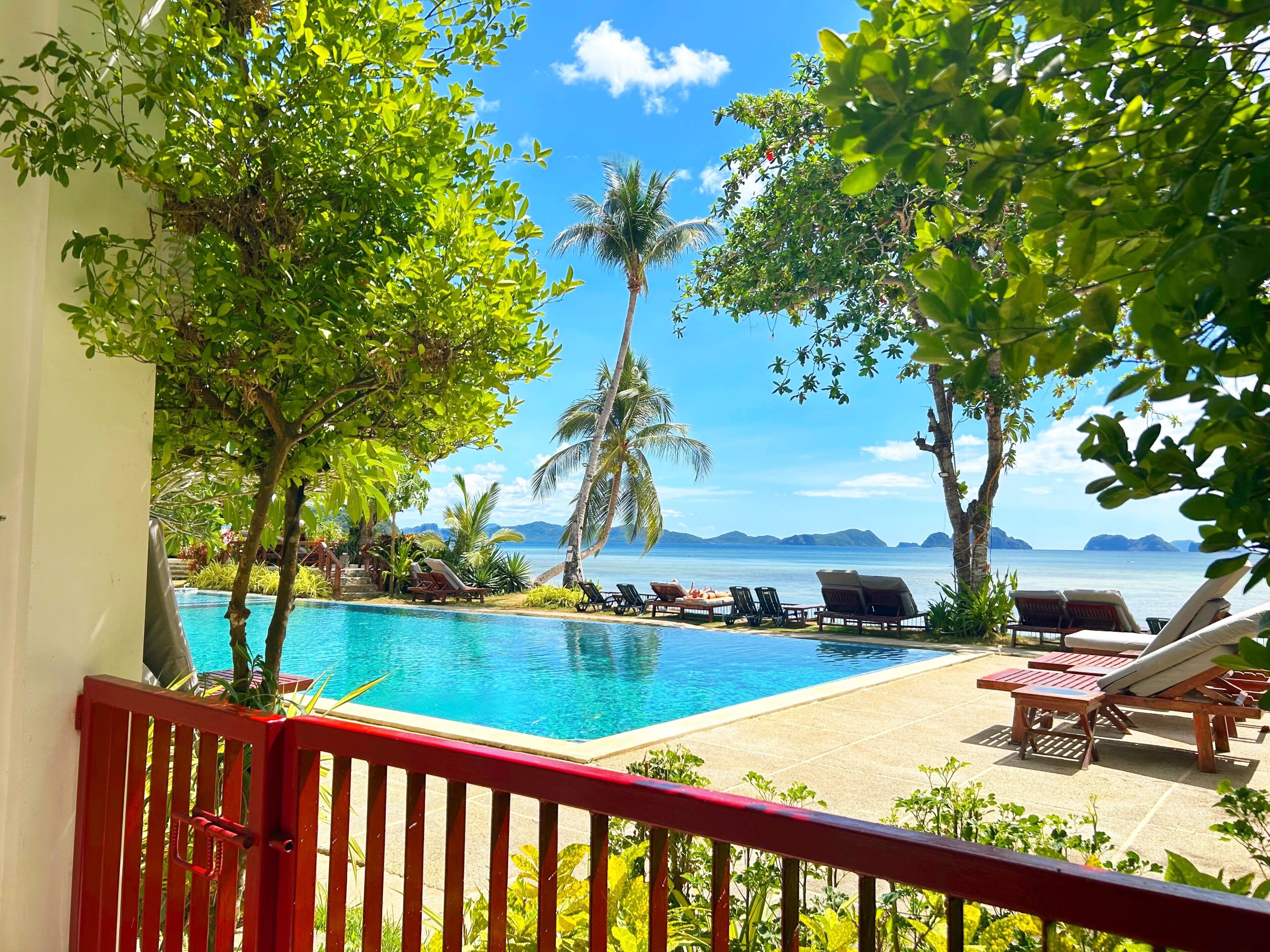 A poolside view with lounge chairs, a clear blue pool, and a view of the ocean and mountains.