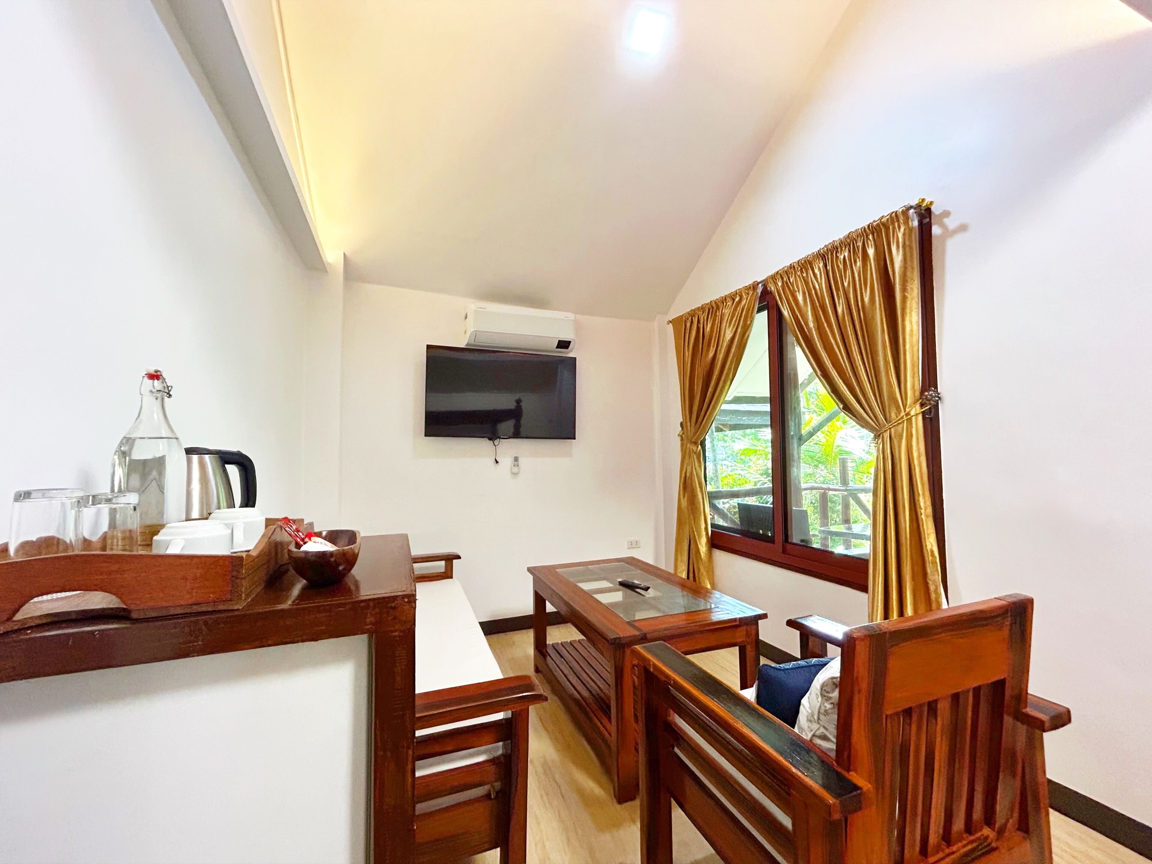 A room with a wooden dining table, chairs, a TV mounted on the wall, and a window with curtains.