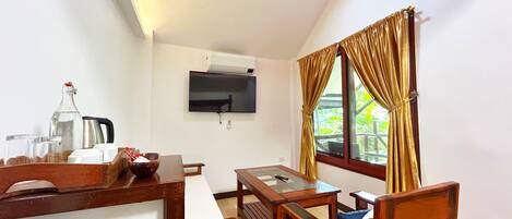 A room with a wooden dining table, chairs, a TV mounted on the wall, and a window with curtains.