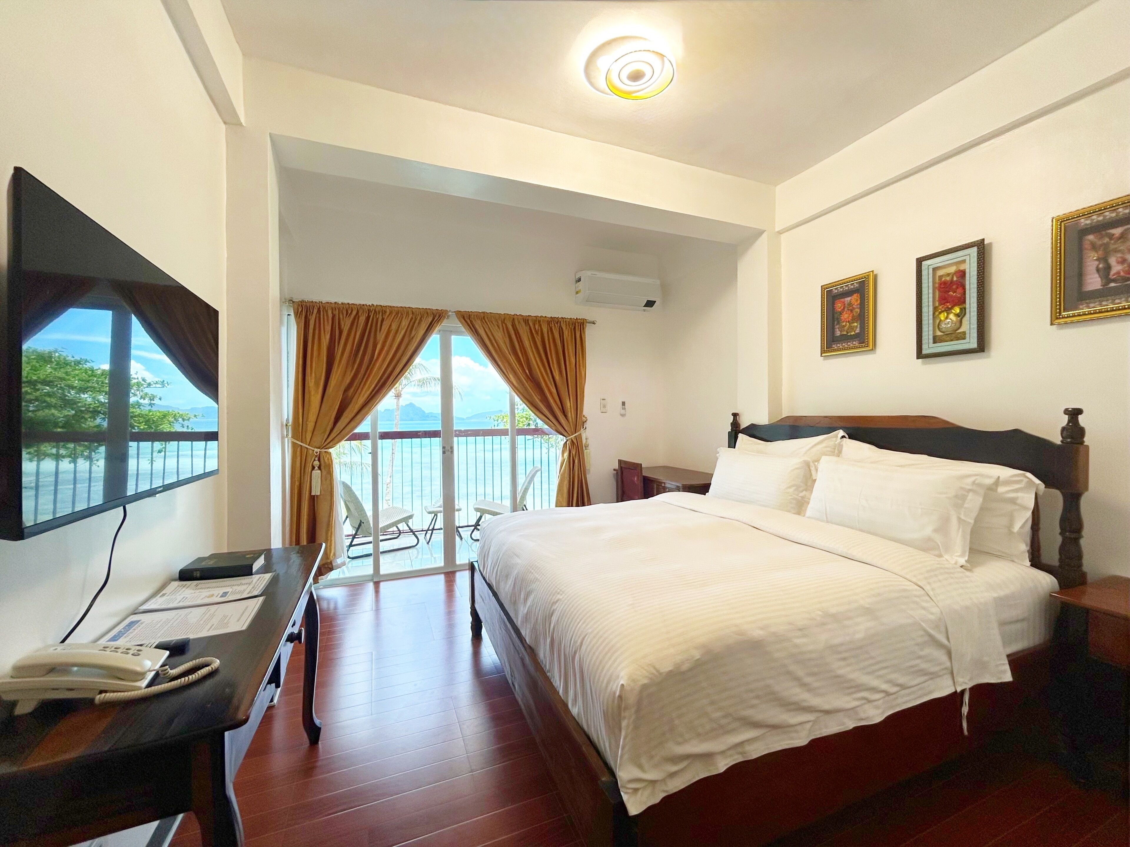A hotel room with a bed, a desk with a phone, a TV, and a balcony with a view.