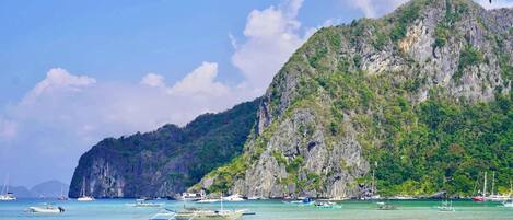 A coastal scene with boats, a mountainous backdrop, and clear skies.