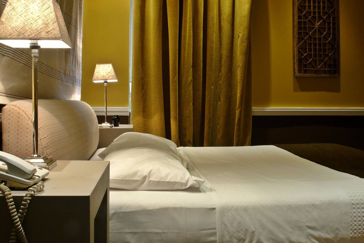 Une chambre d’hôtel avec un lit, deux lampes de chevet, un téléphone et une fenêtre avec des rideaux.