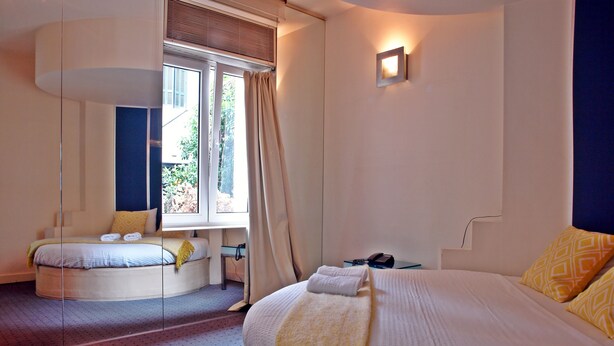 Een moderne hotelkamer met een groot bed, een kleinere zithoek, een bureau en een raam met gordijnen.