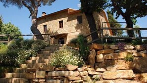 A stone building with a staircase leading up to it, surrounded by greenery and flowers. - La Mulattiera (Scarlino)