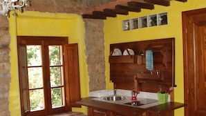 A rustic kitchen with a stone wall, wooden cabinets, and a yellow accent wall. - La Mulattiera (Scarlino)