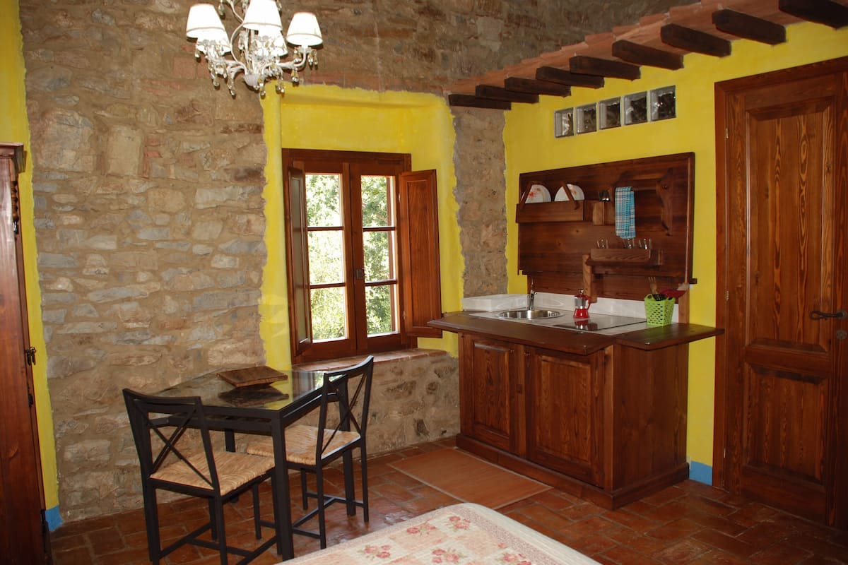 Una cocina con pared de piedra, armarios de madera, una mesa de comedor con sillas y una ventana con vistas a follaje.