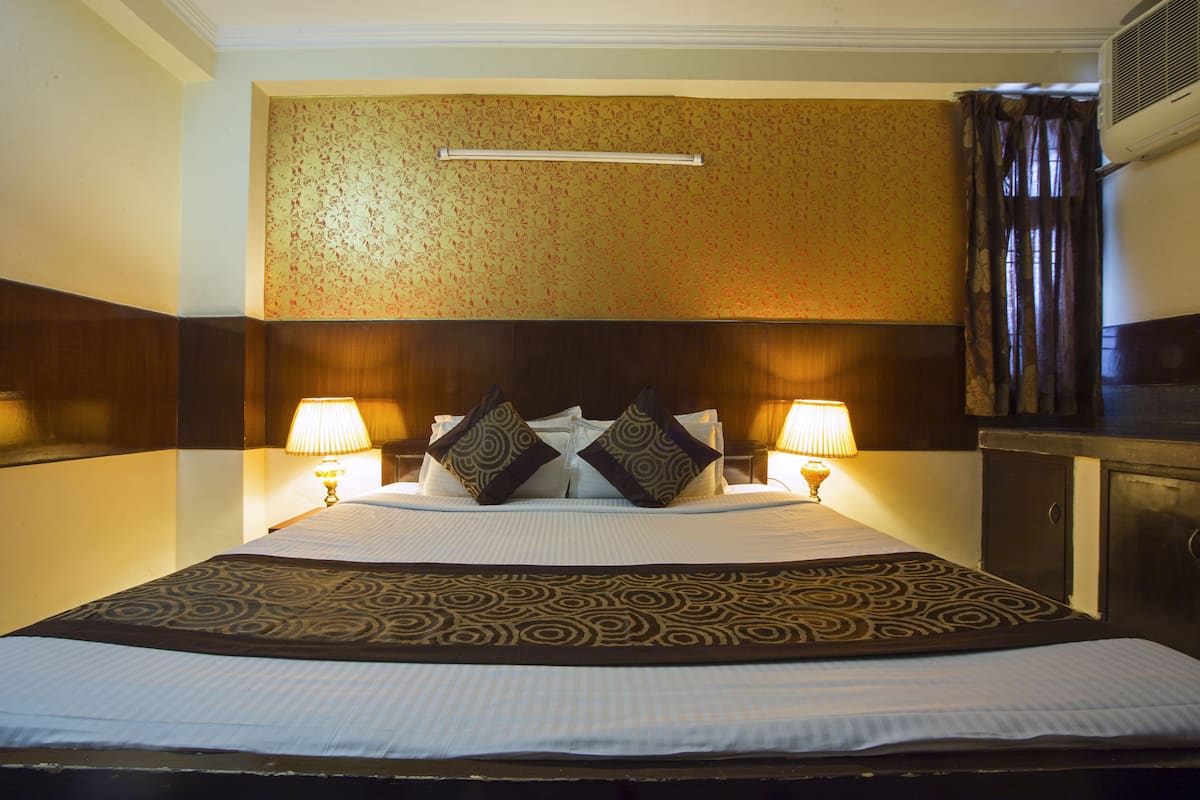 Een hotelkamer met een groot bed, twee bedlampen, een hoofdeinde en een wandgemonteerde airconditioner.