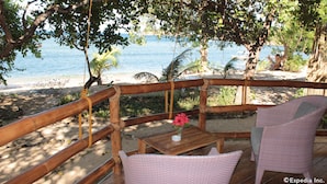 A wooden deck with a view of the beach and ocean. There are wicker chairs and a small table with a vase of flowers. - Cashew Grove Beach Resort (Busuanga)