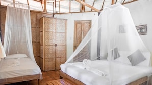 A room with two beds, each with a canopy. There is a wooden wardrobe and a door in the background. - Cashew Grove Beach Resort (Busuanga)