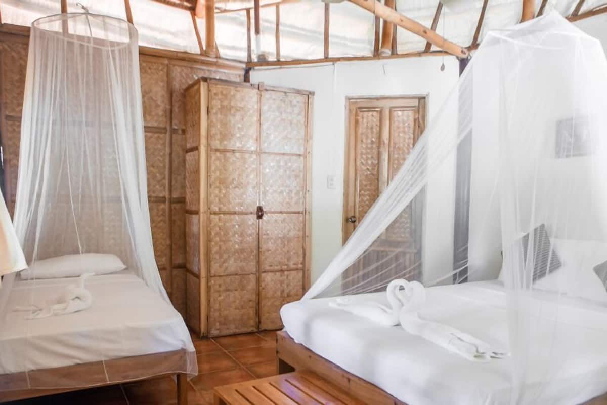 Una habitación con dos camas, cada una con dosel. Se observa un armario de madera y una puerta al fondo.