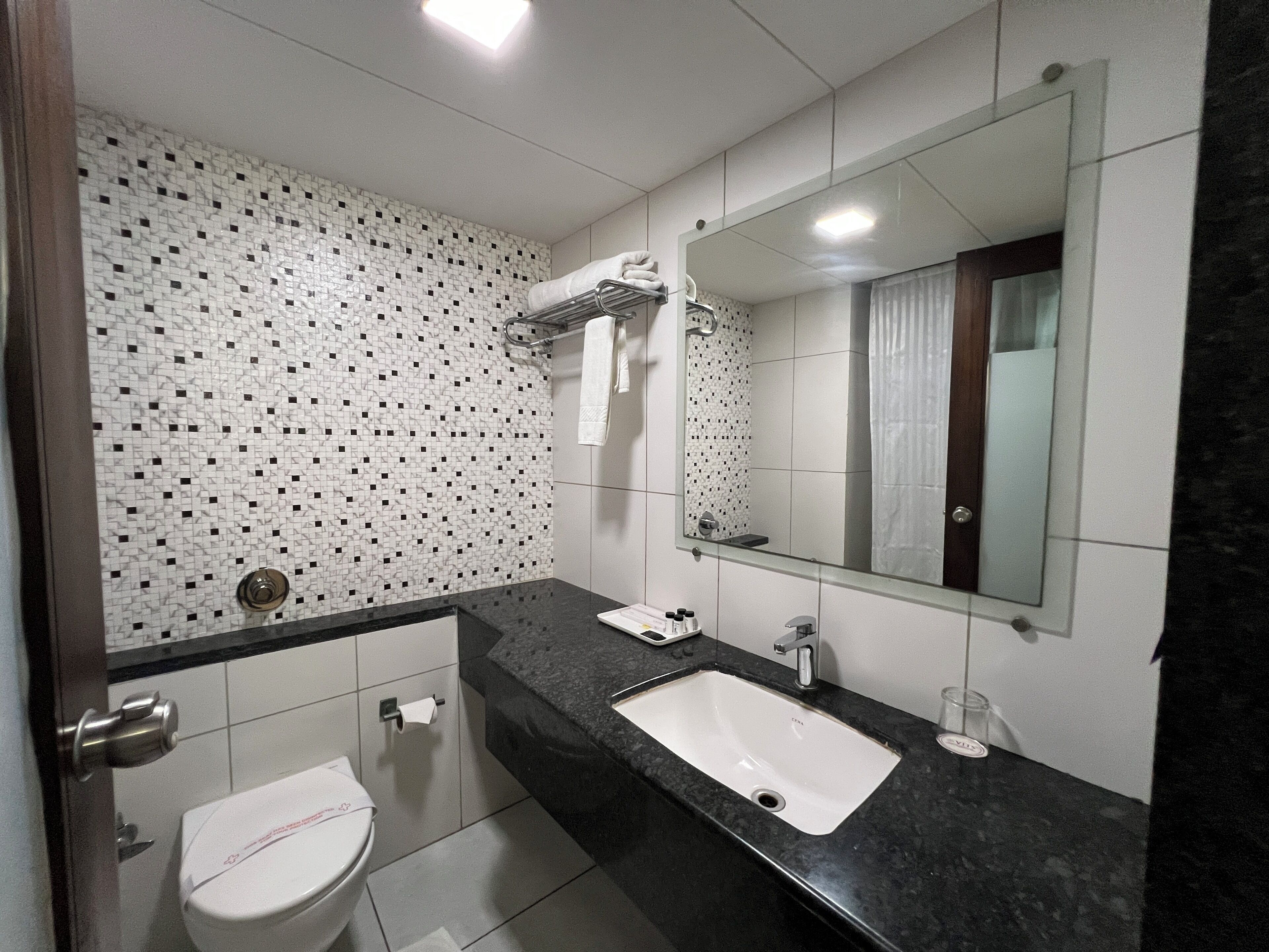 A modern bathroom with a tiled backsplash, a large mirror, a sink, and a toilet.