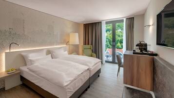 Een hotelkamer met een groot bed, een bureau, een stoel en uitzicht op groen buiten het raam.