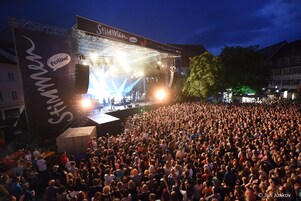 Un escenario de conciertos grande al aire libre con una multitud de personas frente a él.
